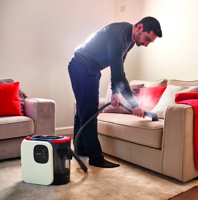 un uomo che pulisce un divano con la forza del vapore del lavatessuti Polti