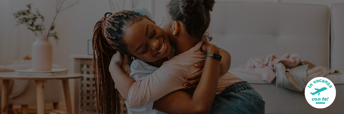 L'immagine mostra mamma e figlia che si abbracciano felici mentre fanno la valigia. In vacanza con te.